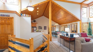 Un intérieur chaleureux avec un plafond en bois, un lit doté d’une tête de lit à rayures, un canapé et un coin repas.