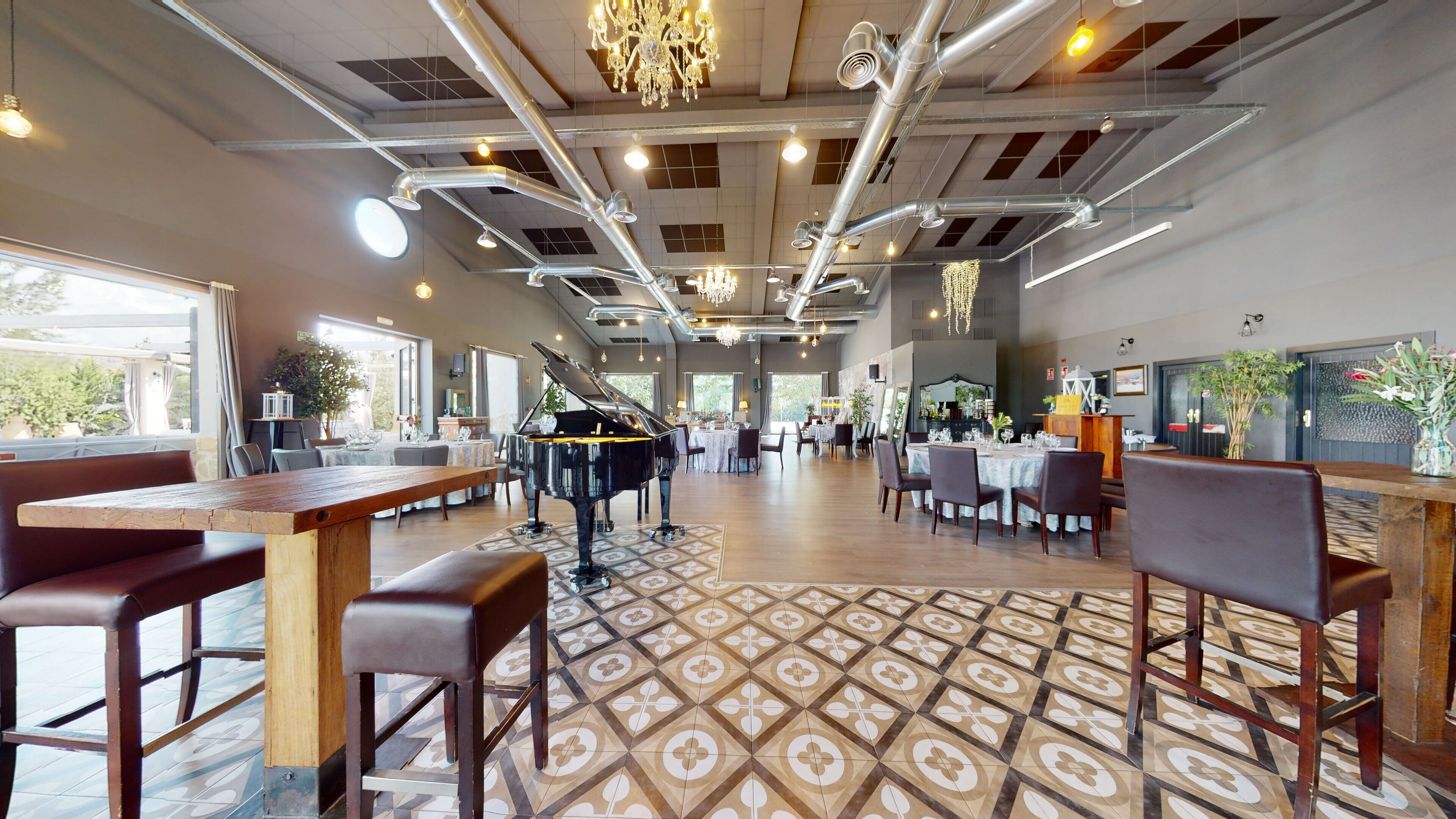 A spacious restaurant with a grand piano, high ceilings with exposed ductwork, and a patterned tile floor.