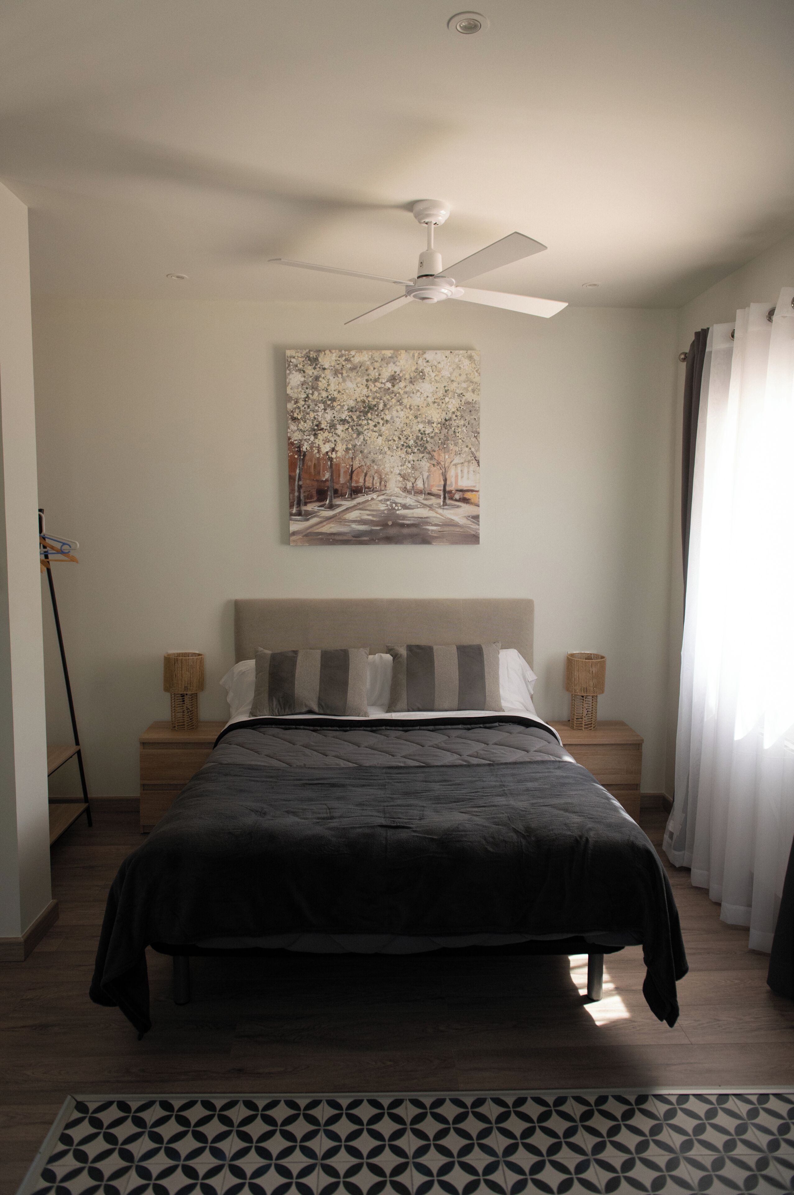 Quarto com cama, ventilador de teto, pintura na parede e mesa de cabeceira com abajur.