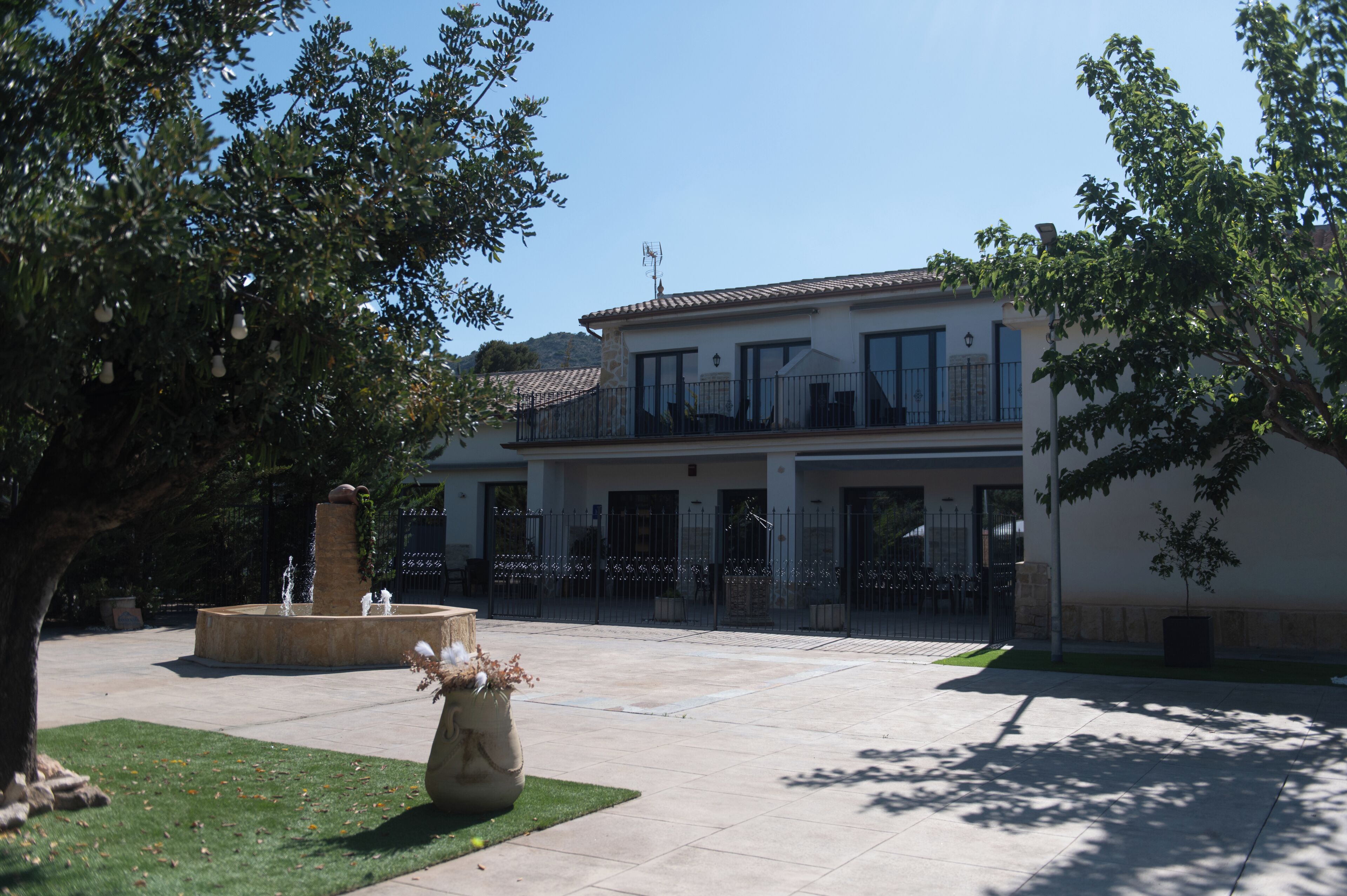 Un edificio de dos pisos con un balcón, una fuente y un patio empedrado.