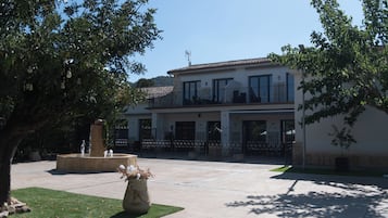 Un edificio de dos pisos con un balcón, una fuente y un patio empedrado.