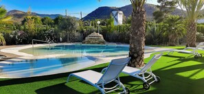 A pool area with lounge chairs, a stone fountain, and a mountainous backdrop. - Bellevall hotel  (Aspe)