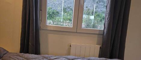 Een slaapkamer met een groot bed, een raam met gordijnen en een radiator.