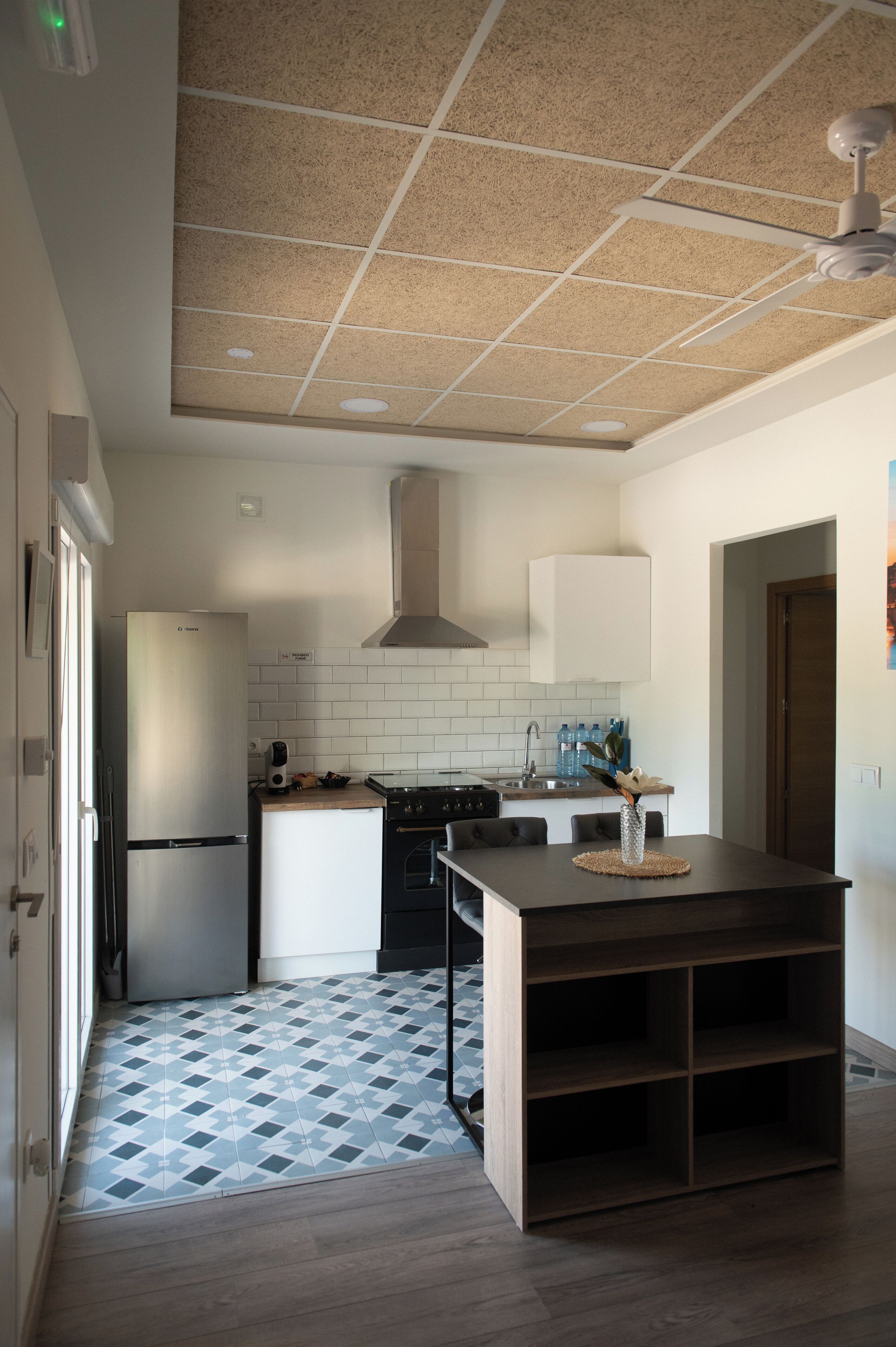 Une cuisine avec un sol carrelé, un réfrigérateur, une cuisinière et un ventilateur de plafond.