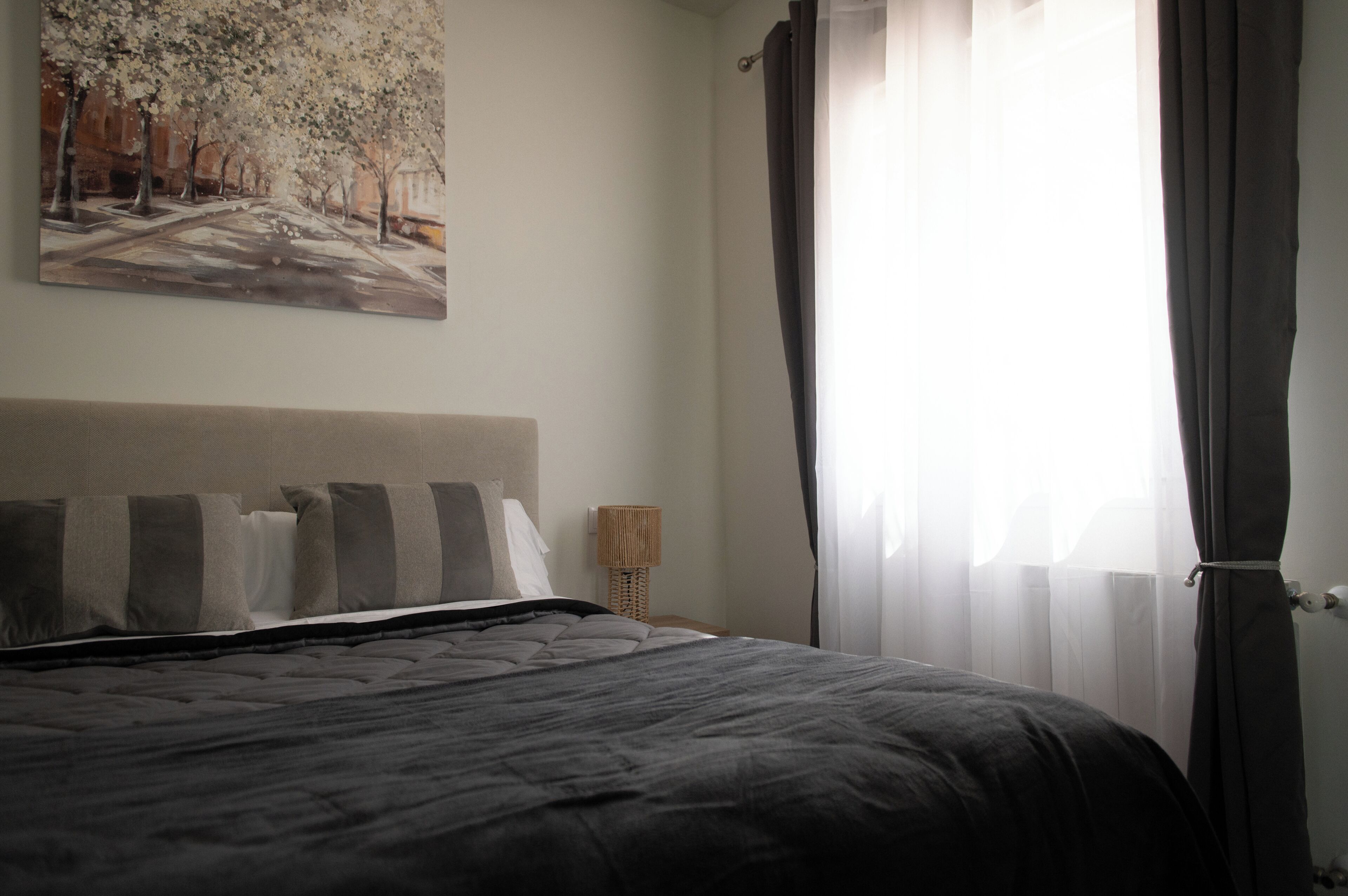 A bedroom with a bed, a lamp, a painting, and a window with curtains.