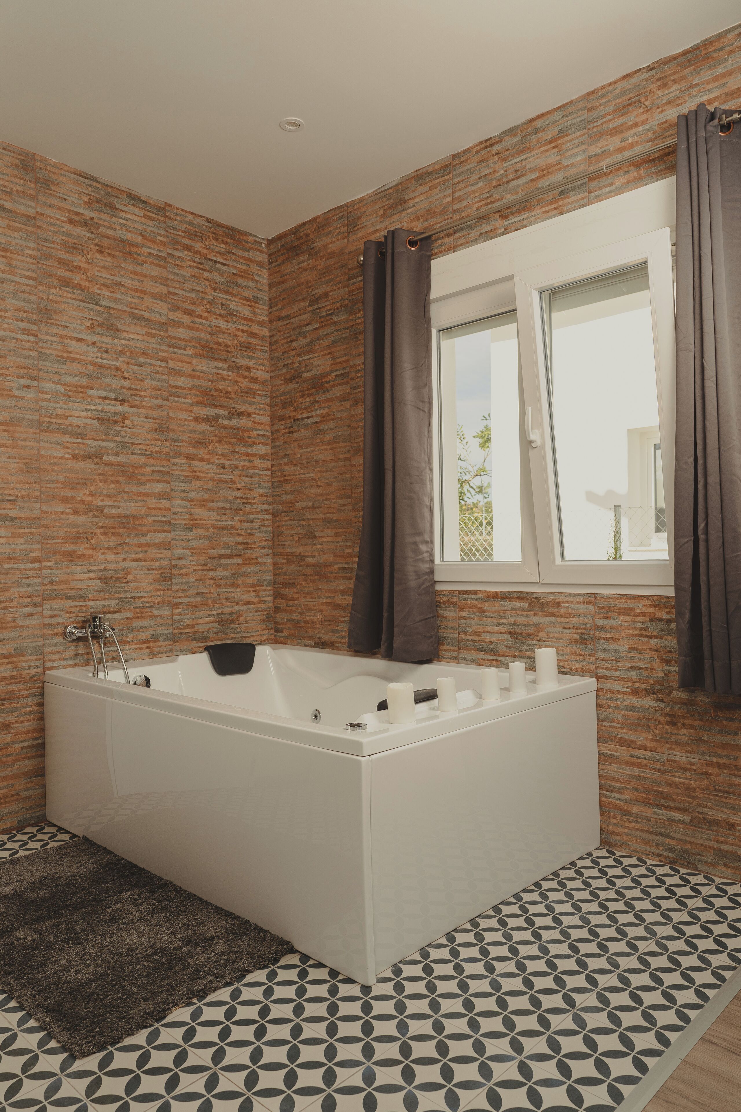 A modern bathroom with a freestanding bathtub, a window with curtains, and patterned floor tiles.