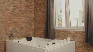 A modern bathroom with a freestanding bathtub, a window with curtains, and patterned floor tiles.