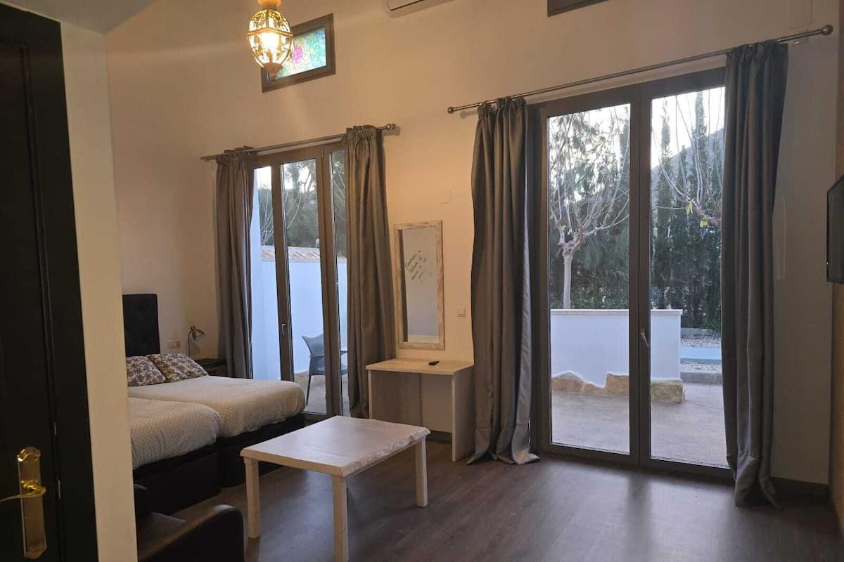 A room with a bed, a small table, and a view through large sliding glass doors.