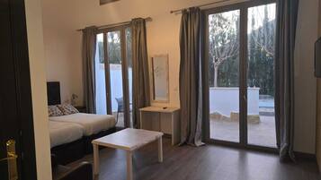 A room with a bed, a small table, and a view through large sliding glass doors.