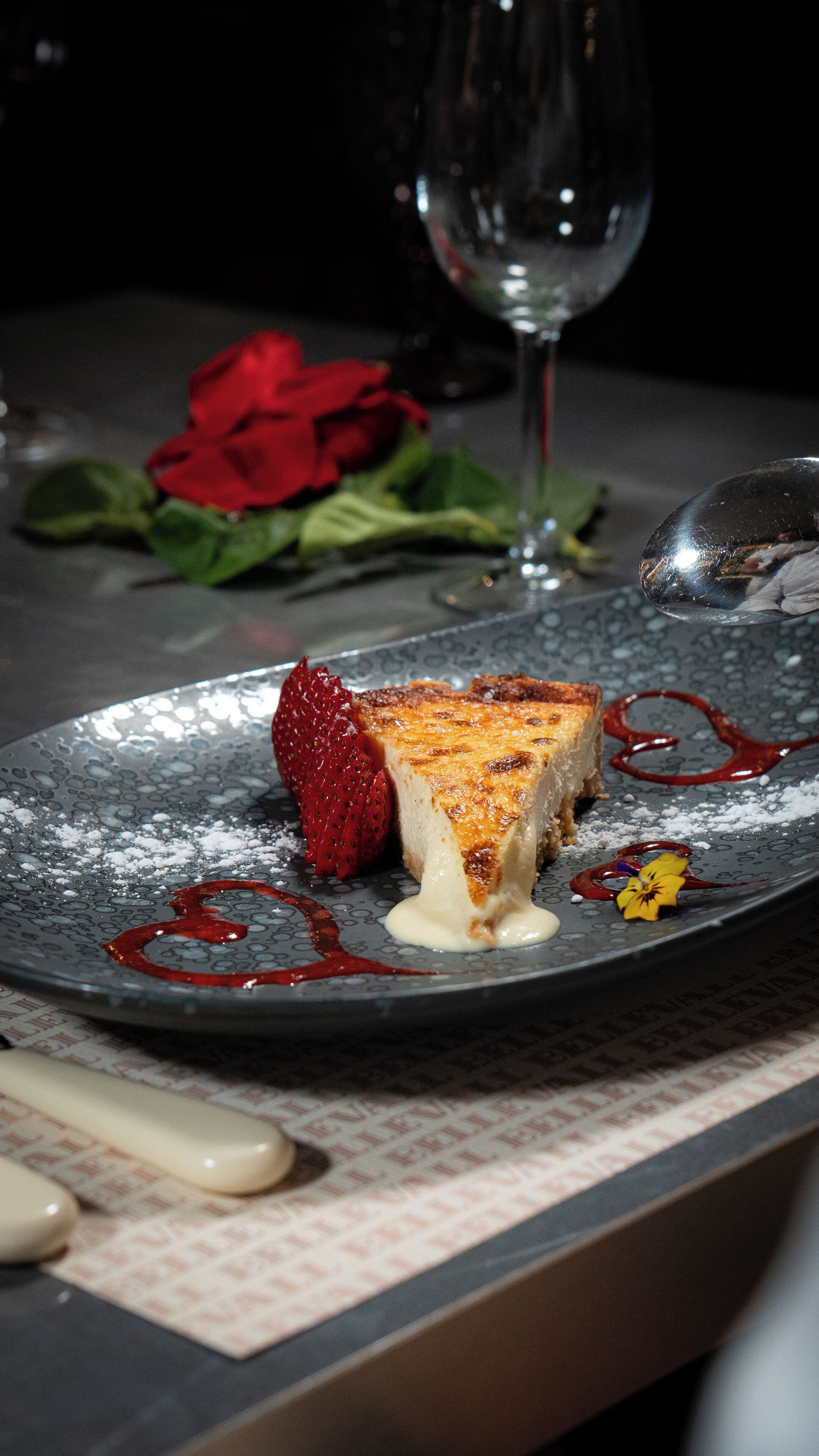 Une assiette à dessert avec une part de gâteau au fromage, une fraise et une sauce rouge.