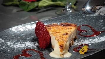 Une assiette à dessert avec une part de gâteau au fromage, une fraise et une sauce rouge.