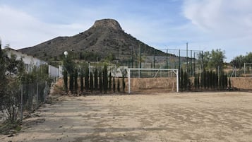 Un campo de fútbol con un arco, rodeado de una valla y árboles, con una montaña al fondo.
