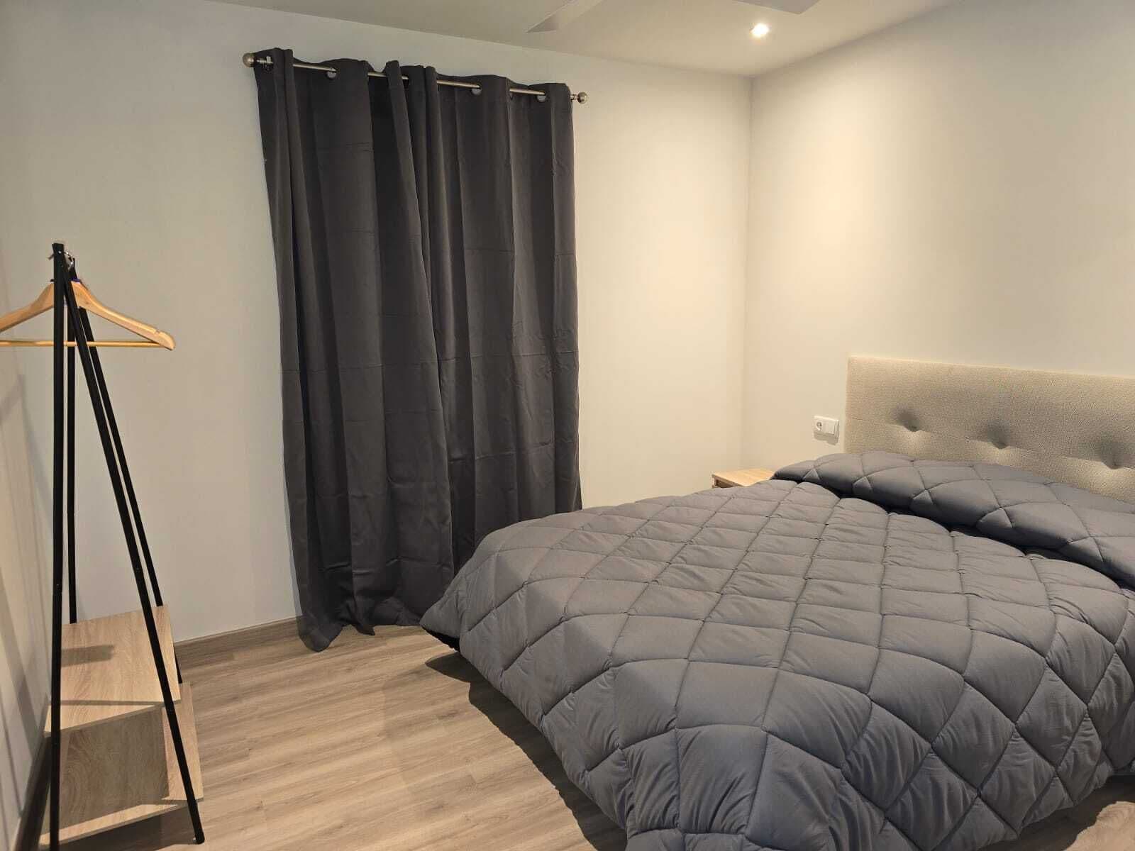 Une chambre à coucher avec un lit, un plancher en bois, une tête de lit et un rideau.