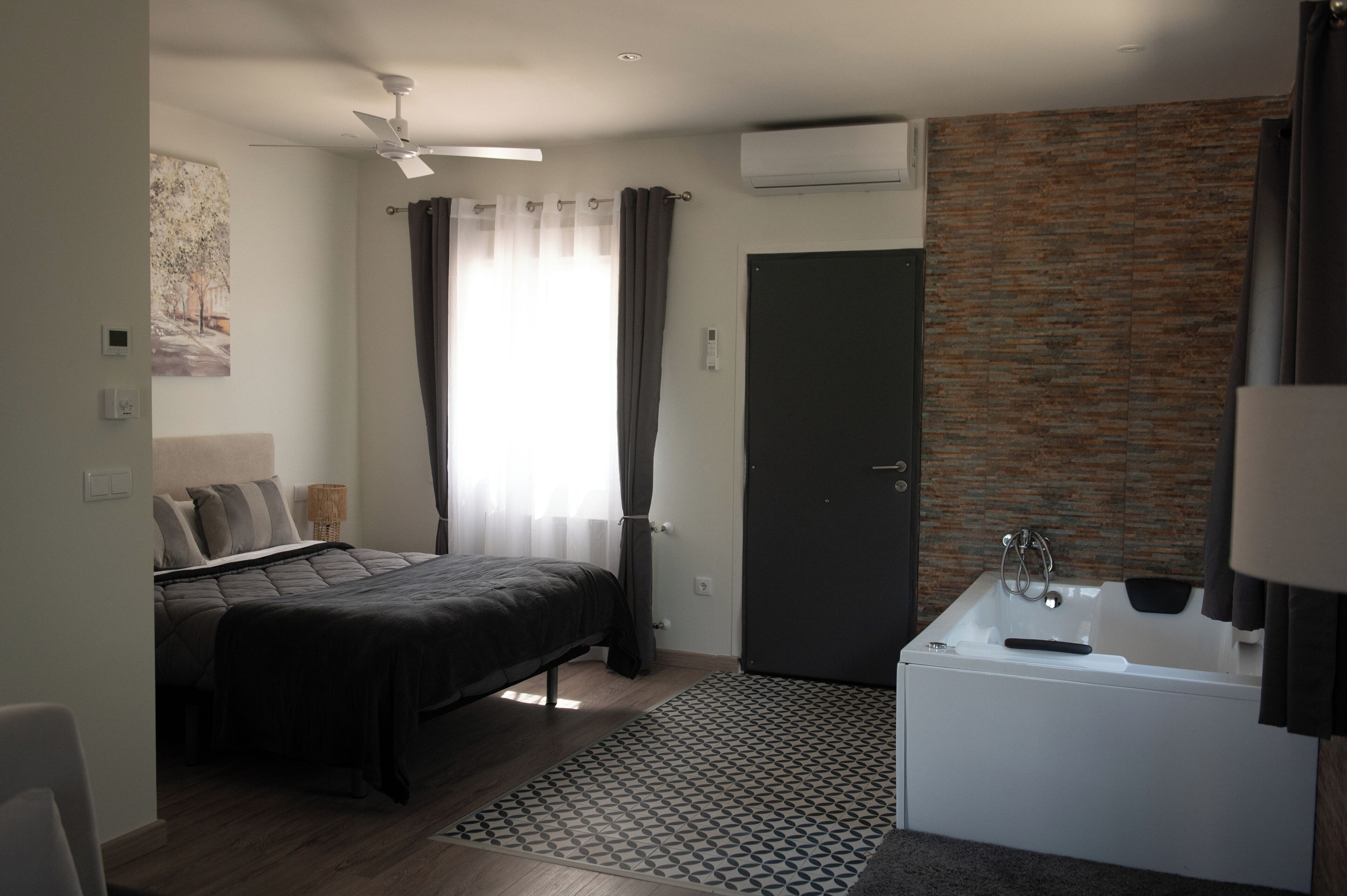 Un dormitorio moderno con cama, ventilador de techo, ventana con cortinas y baño con bañera y ducha.