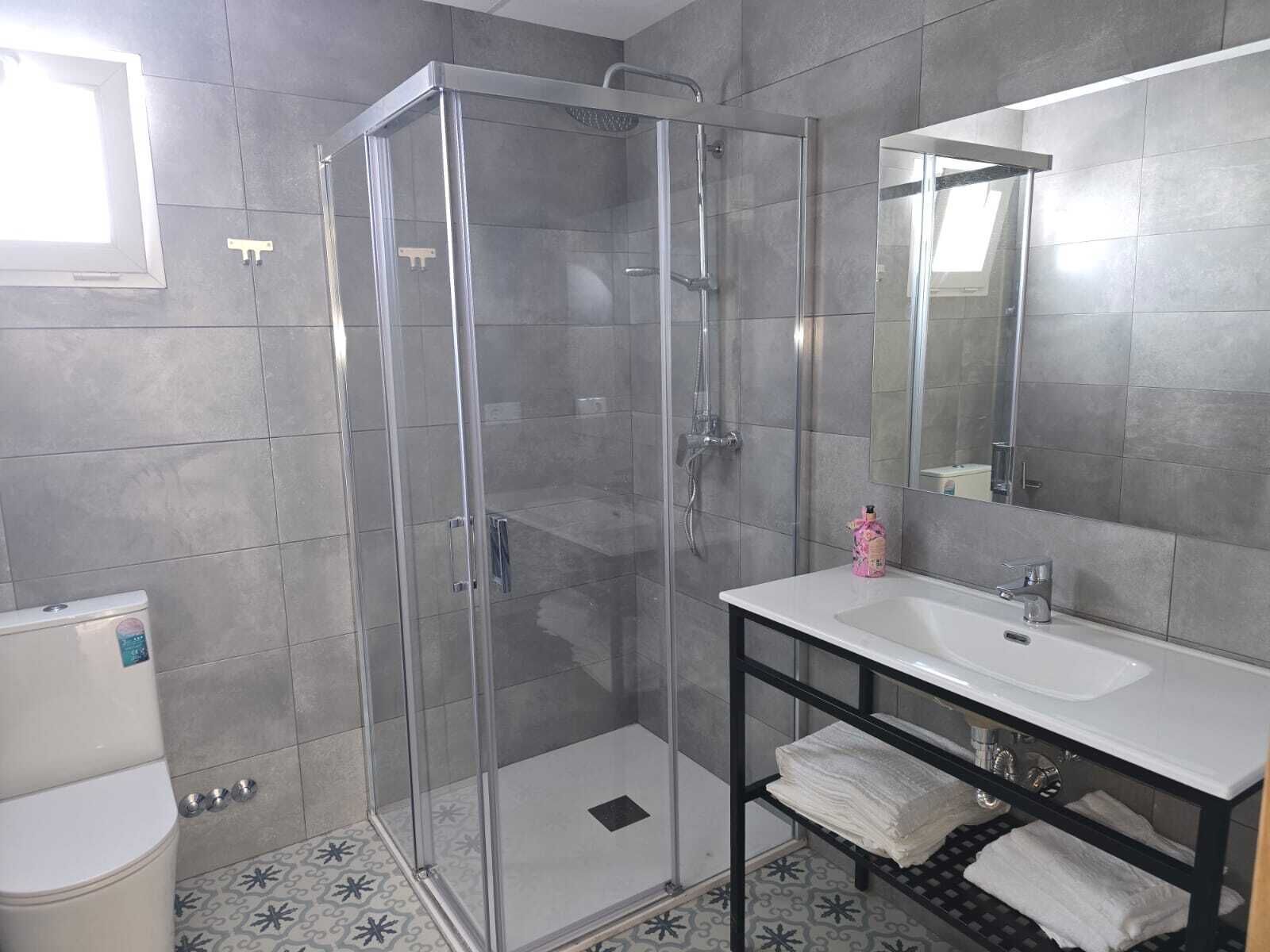 Une salle de bain moderne avec une douche à l’italienne en verre, un lavabo blanc et un miroir au-dessus.