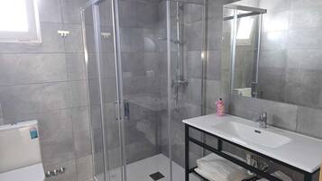 Une salle de bain moderne avec une douche à l’italienne en verre, un lavabo blanc et un miroir au-dessus.