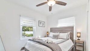 Un dormitorio con cama, dos mesitas de noche, ventilador de techo y ventana con persianas.