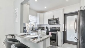 Una cocina moderna con armarios blancos, encimera de granito, electrodomésticos de acero inoxidable y un refrigerador negro.