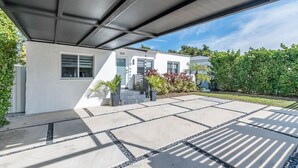 Una casa moderna con un porche cubierto, fachada blanca y un jardín bien cuidado.