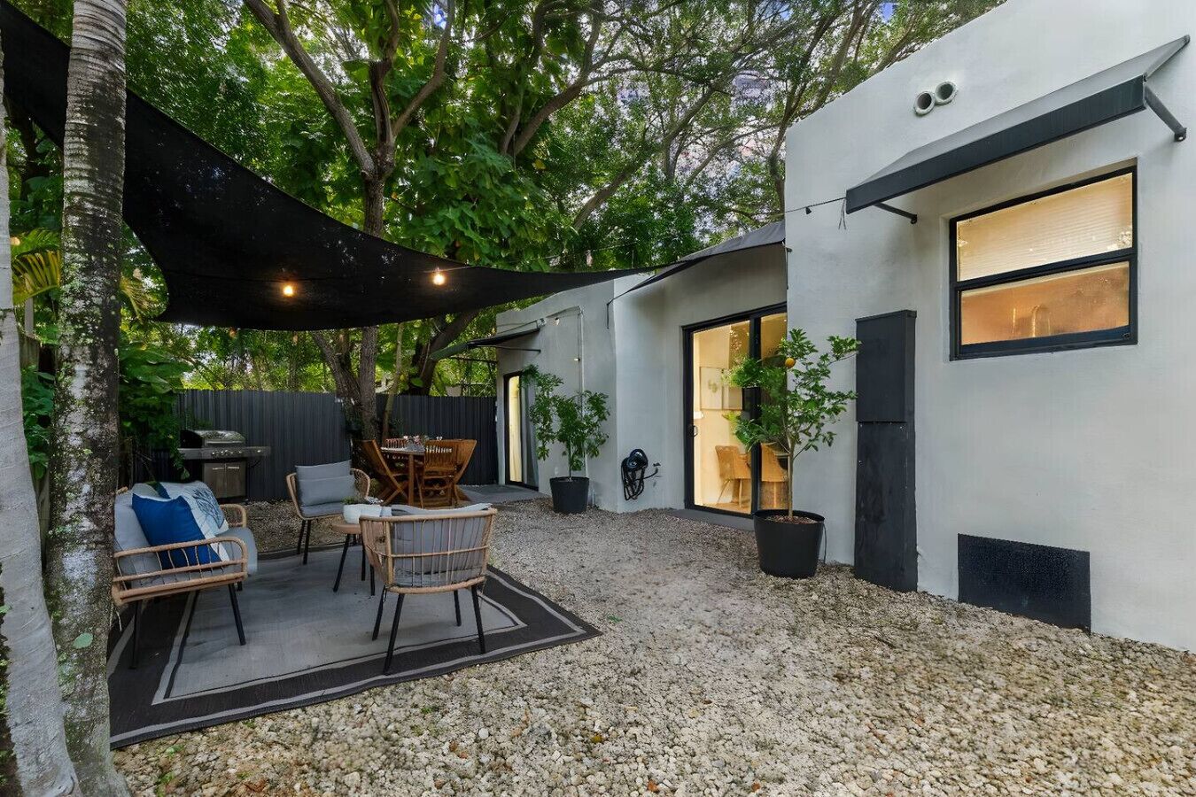 Un patio moderno al aire libre con un comedor, una parrilla y plantas en macetas.