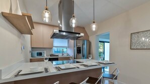 Une cuisine moderne dotée d’un îlot central, d’appareils électroménagers en acier inoxydable et de luminaires suspendus.