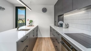 A modern kitchen with a white countertop, grey cabinets, a wooden floor, and a view of a mountain through a window. - Private Balcony, 2 Bathroom, Free Washer Dryer (Wānaka)