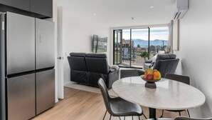 A modern kitchen with a built-in refrigerator, a dining area with a round table and chairs, and a balcony with a view of the mountains. - Private Balcony, 2 Bathroom, Free Washer Dryer (Wānaka)