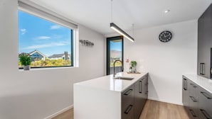 A modern kitchen with a large island, a window with a view, and a clock on the wall. - Private Balcony, 2 Bathroom, Free Washer Dryer (Wānaka)