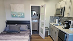 A compact bedroom with a bed, a small kitchenette, and a bathroom visible through an open door. - Liberty Hill Executive Inn (Zephyrhills)