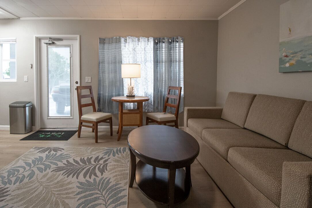 A living room with a sofa, two chairs, a small table, a lamp, and a door.