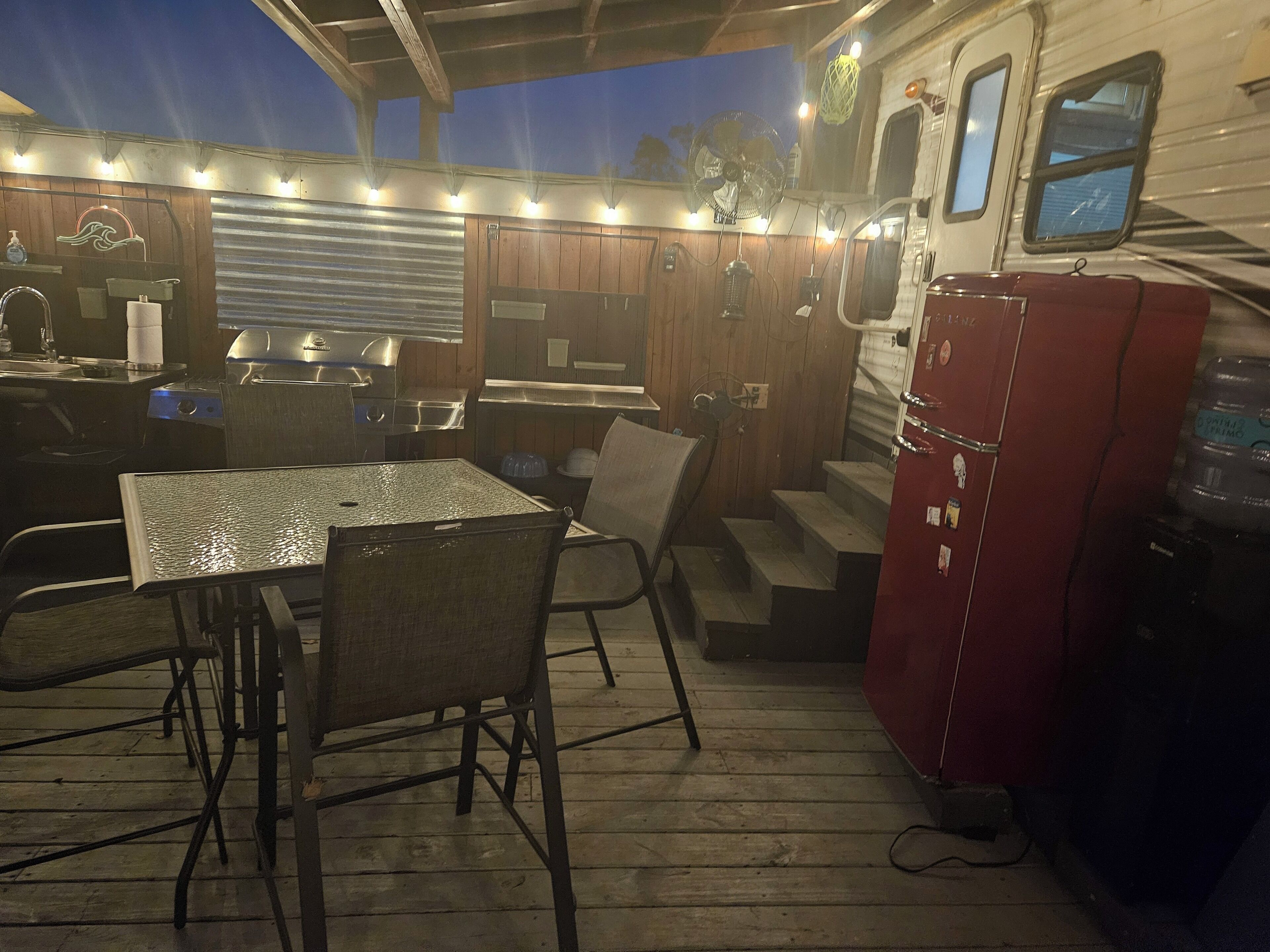 Un'area pranzo all'aperto coperta, con tavolo e sedie, un barbecue e un frigorifero.
