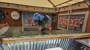 A bar area with a tiled countertop, two cushioned bar stools, a decorative vase with flowers, and a painting on the wall. - Liberty Hill Executive Inn (Zephyrhills)