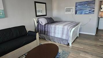 A room with a bed, a sofa, a small table, and a painting on the wall.
