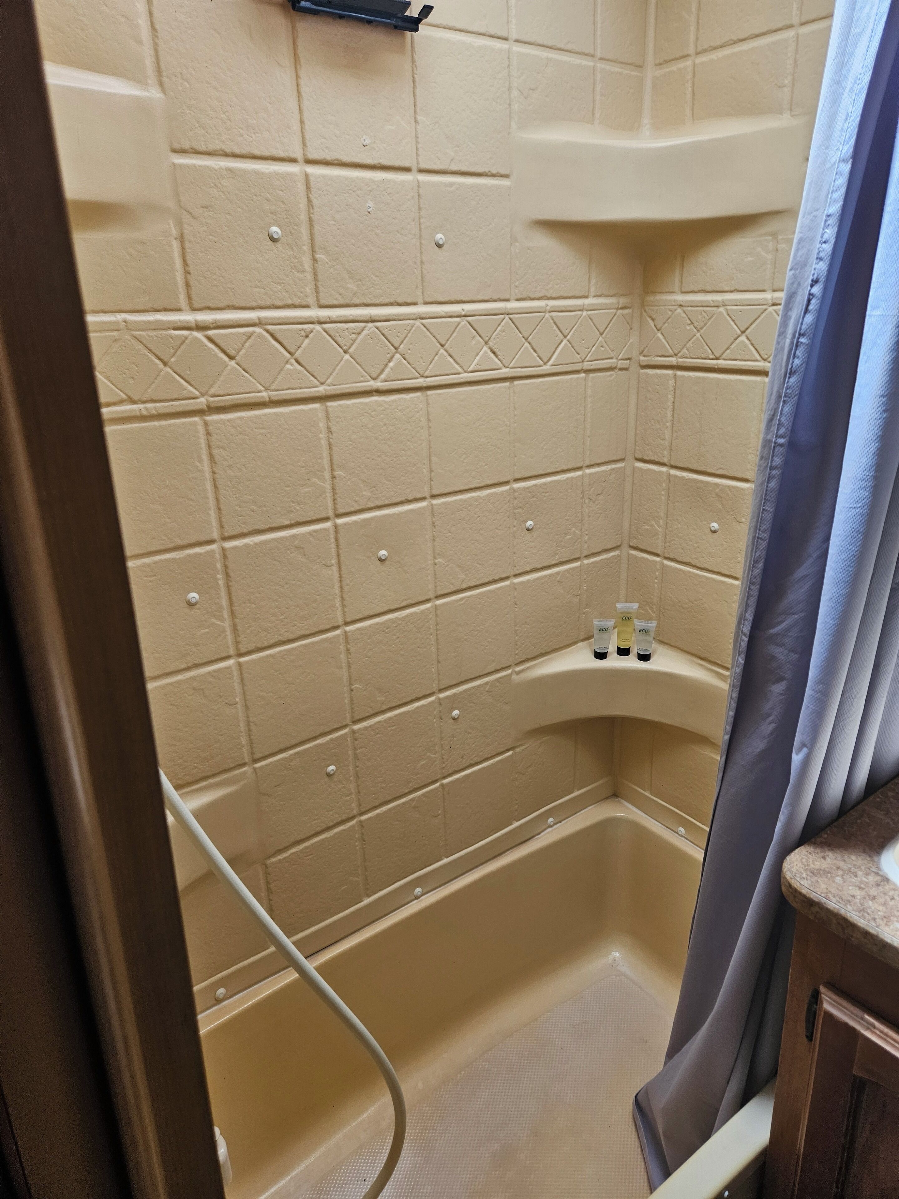 A bathroom with beige tiles, a shower area, and a shelf with toiletries.