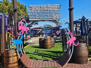 Zona de juegos con un letrero que dice 'Two Naked Monkey's Bar' y una estructura de madera con techo curvo.