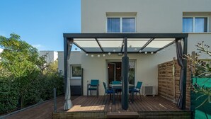 Eine überdachte Terrasse mit Tisch und Stühlen, eine Holzterrasse und der Blick auf ein Haus.