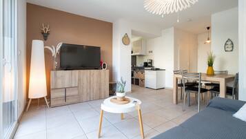 Un salon moderne doté d’un téléviseur à écran plat, d’une table basse ronde et d’un coin repas avec une table et des chaises en bois.