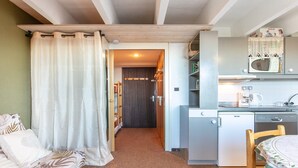 A compact kitchen with a microwave, coffee maker, and a small refrigerator. There is a wooden dining table with a patterned tablecloth. - Apartment with Ski Access (Chamrousse)