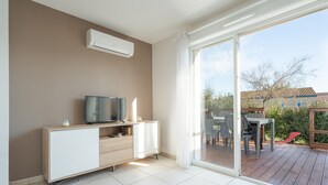 A modern living room with a TV, a cabinet, and a sliding glass door leading to an outdoor deck. - Bright Villa Steps from the Sea (Sérignan)