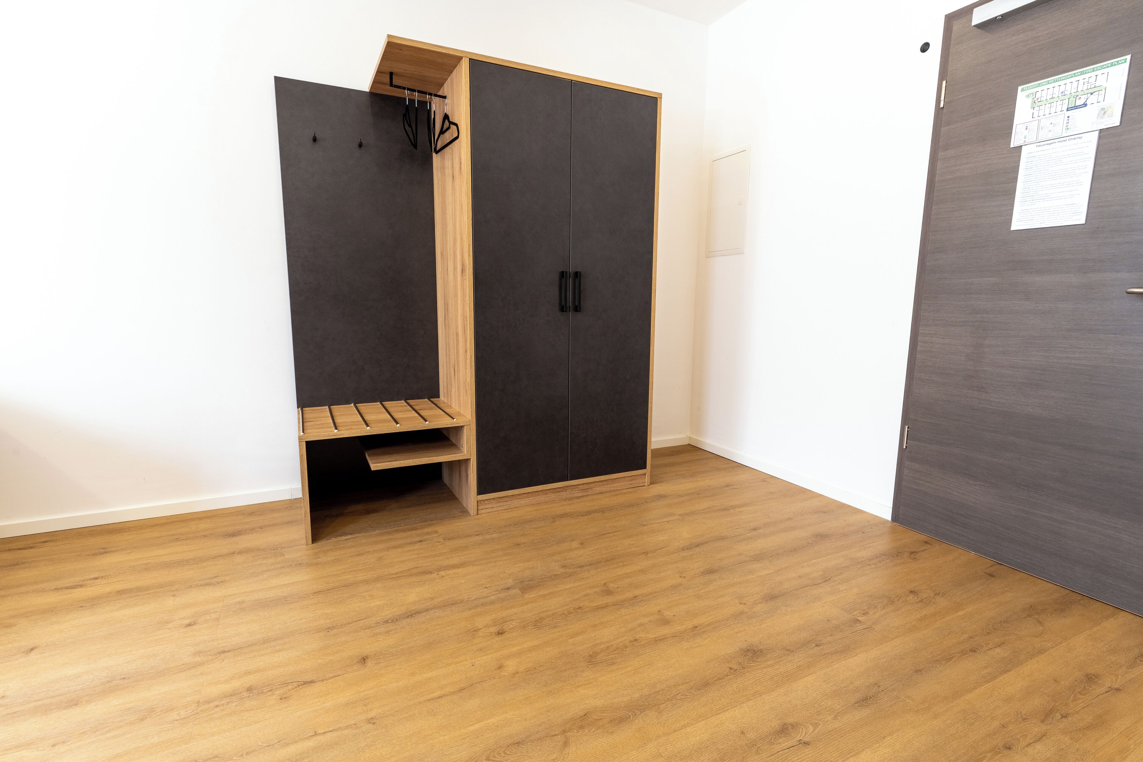 Een kamer met een houten bankje, een garderobe en een deur met een berichtje erop.