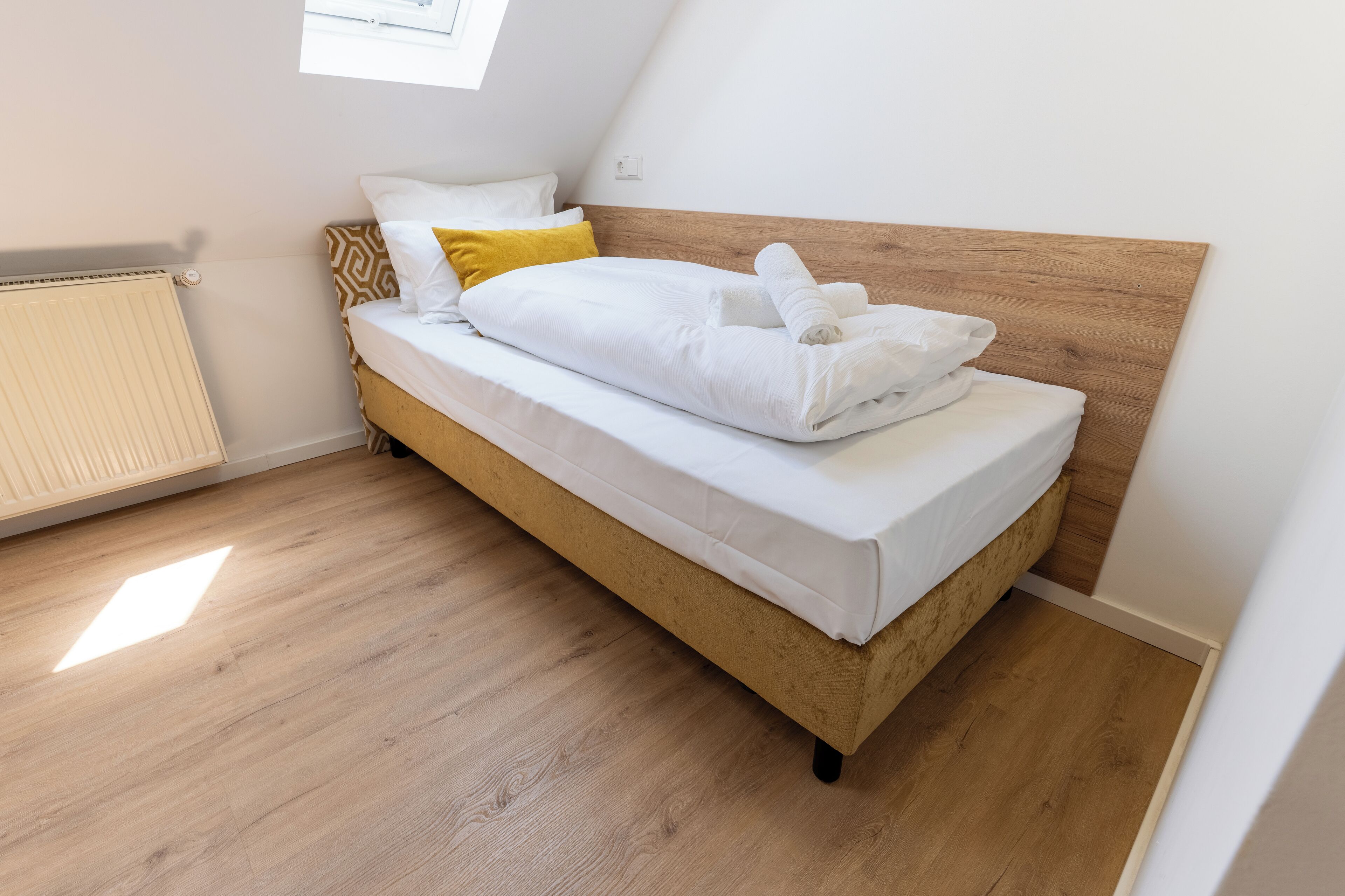A single bed with a wooden headboard, white bedding, and a yellow pillow.