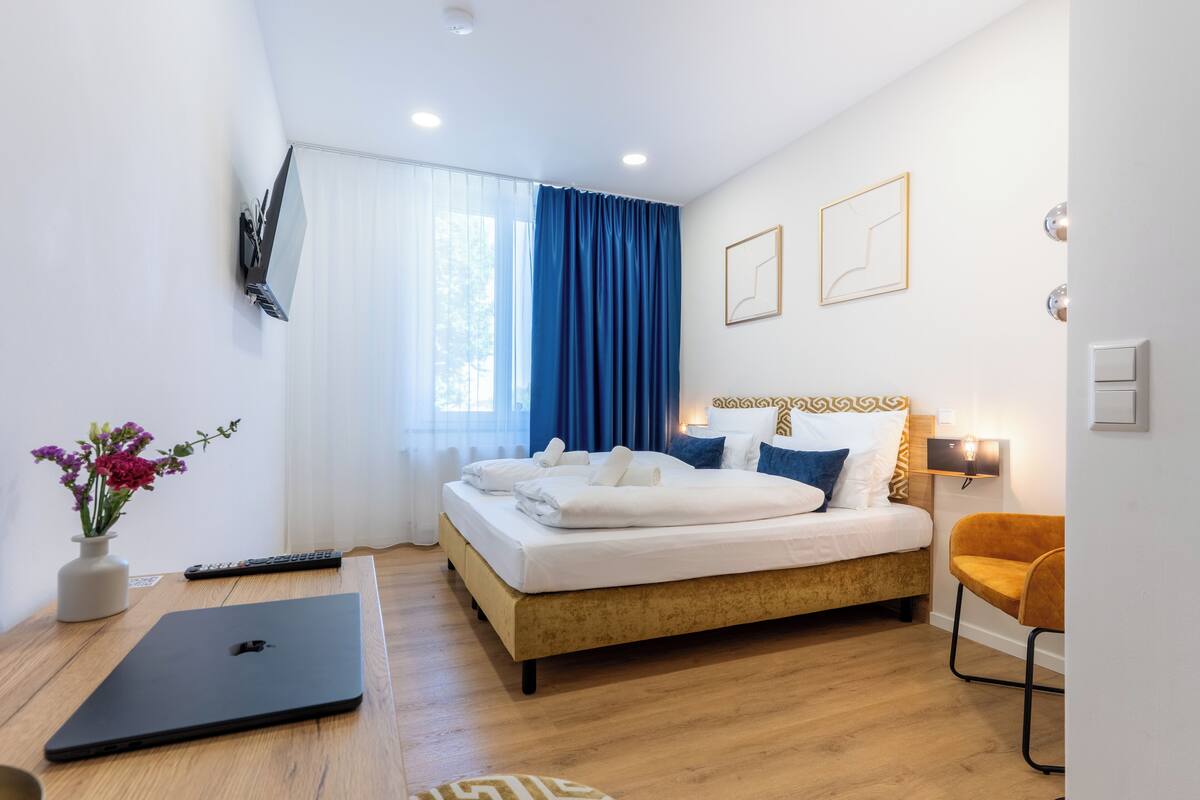 Een moderne hotelkamer met een bed, een bureau met een laptop, een stoel en een bloemenvaas.