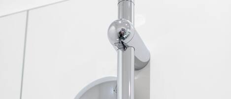 Un pommeau de douche chromé, muni d’un flexible, est fixé sur un mur recouvert de carreaux blancs.