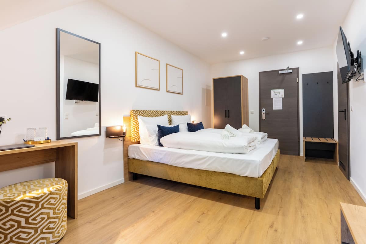 Een moderne hotelkamer met een bed, nachtkastje, spiegel, kledingkast en een televisie.