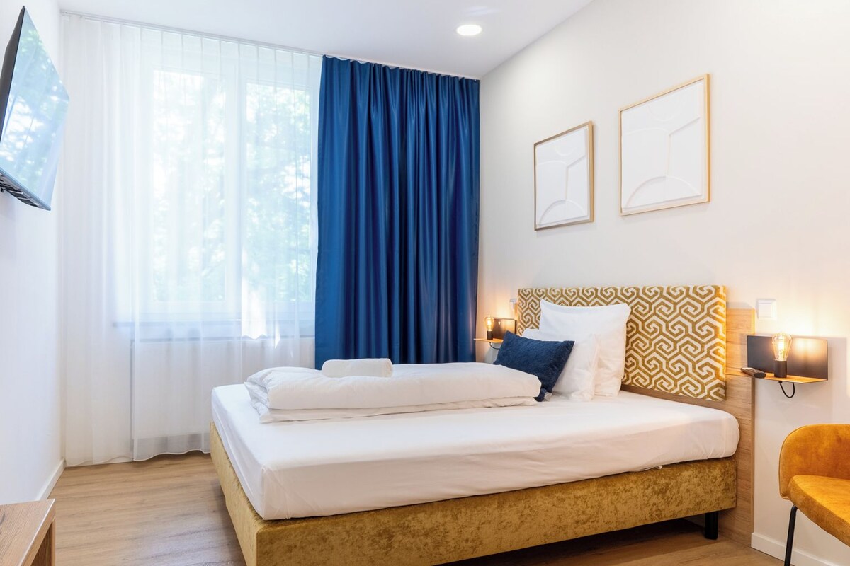 A hotel room with a bed, a desk, a chair, and a TV on the wall.