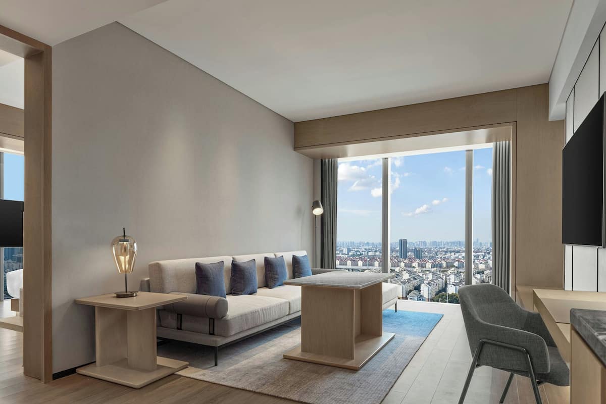 Un salon moderne avec un canapé, une table basse et un fauteuil. Il est doté de grandes fenêtres offrant une vue sur la ville.