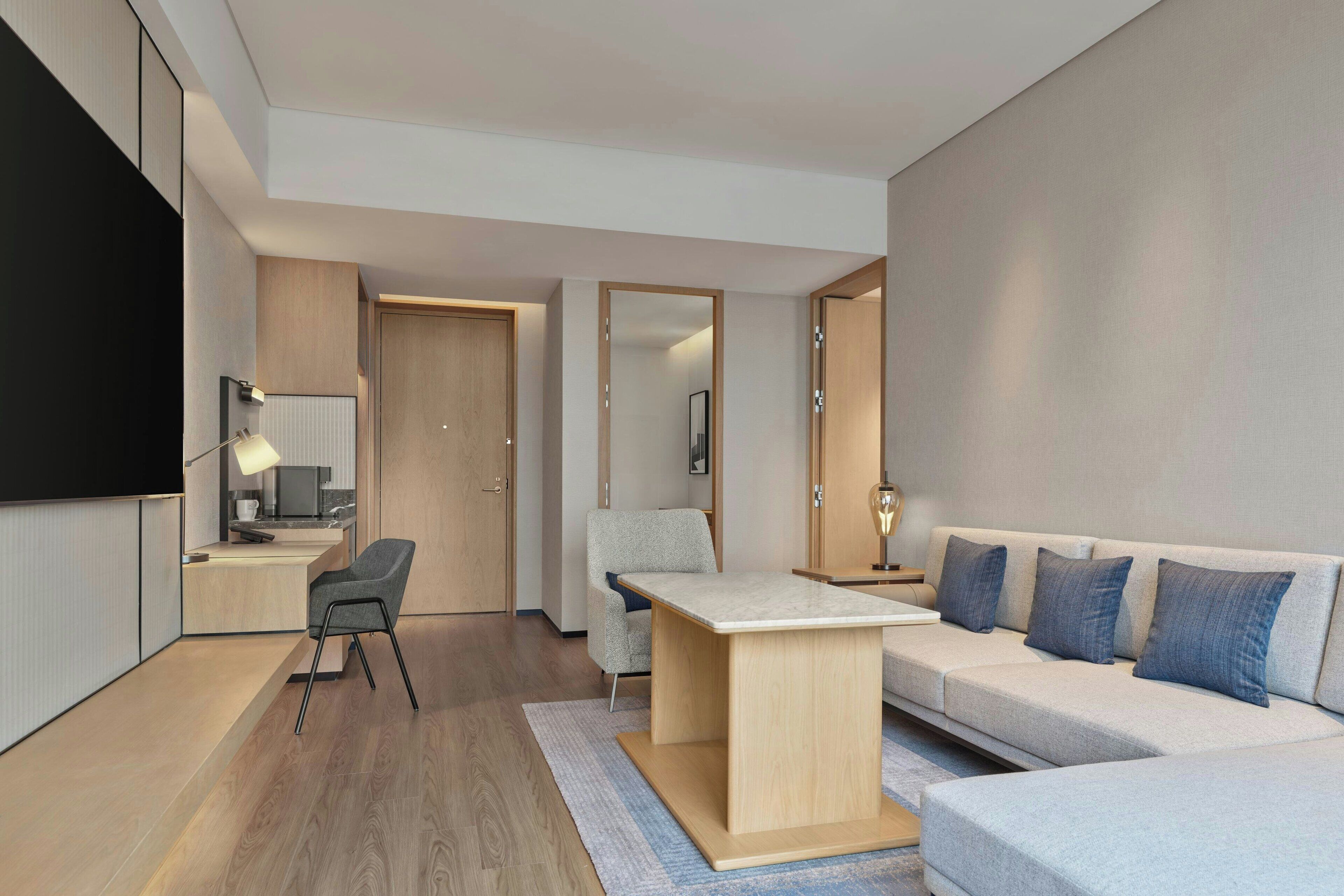 Habitación de hotel moderna con sofá, escritorio, silla, televisor y espejo.
