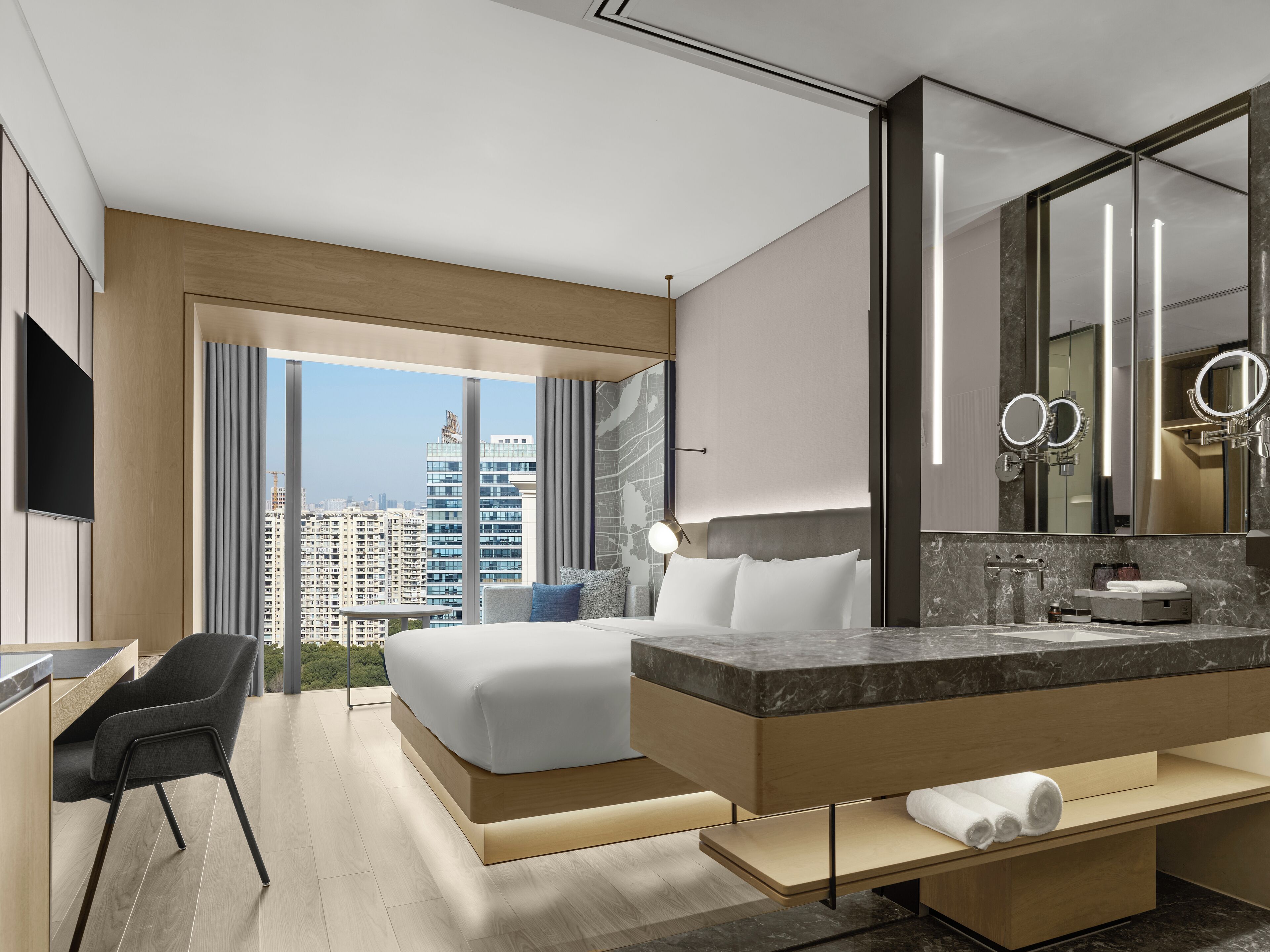 A modern hotel room with a large bed, a bathroom with a marble countertop, and a city view.