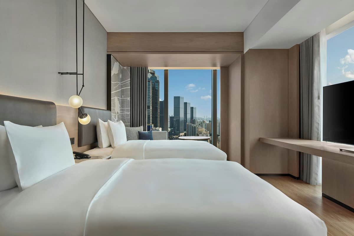 Une chambre d’hôtel moderne avec deux lits, une vue sur la ville, un téléviseur à écran plat et une petite table.