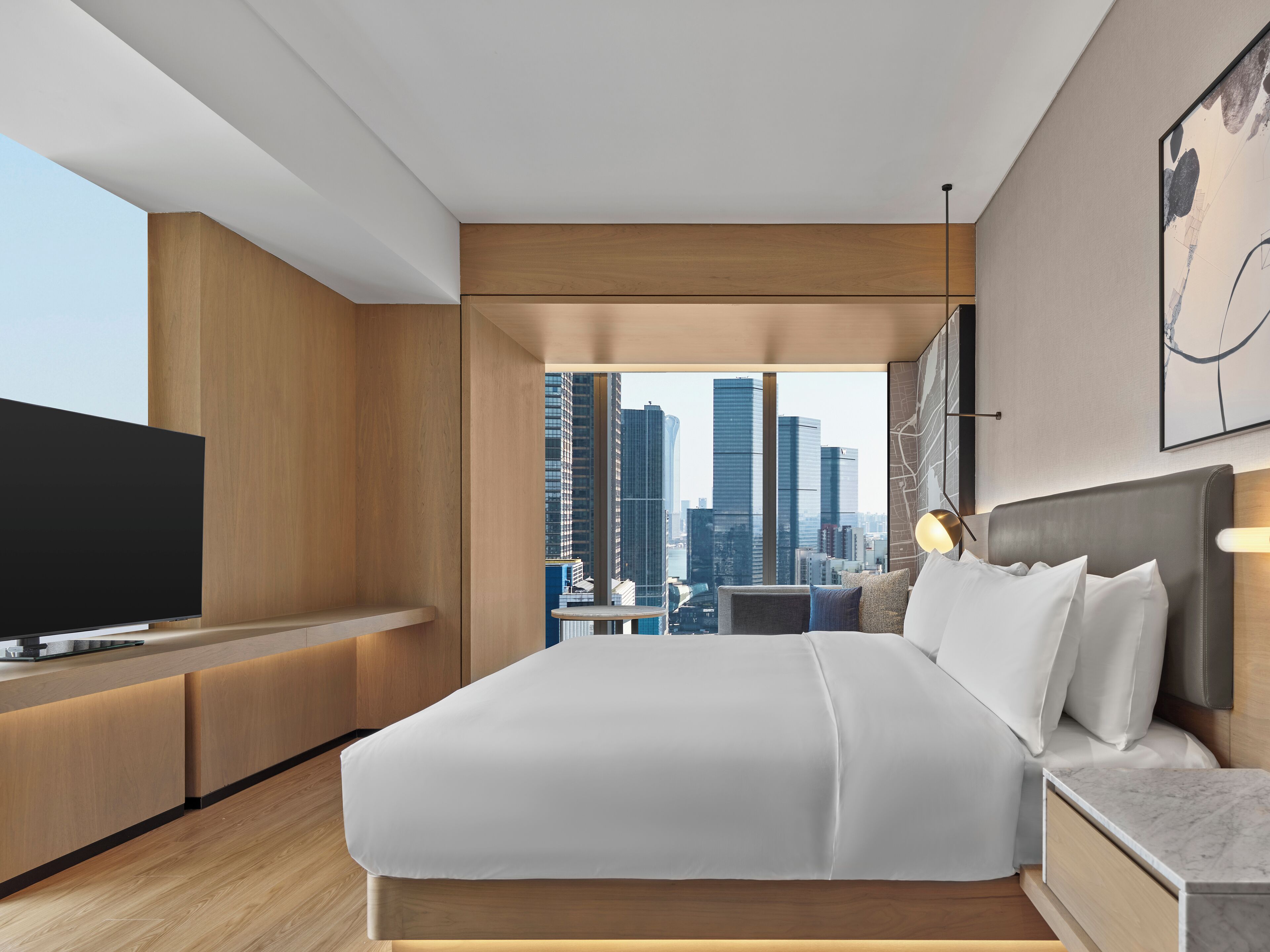 A modern hotel room with a large bed, a TV, a desk, and a city view.